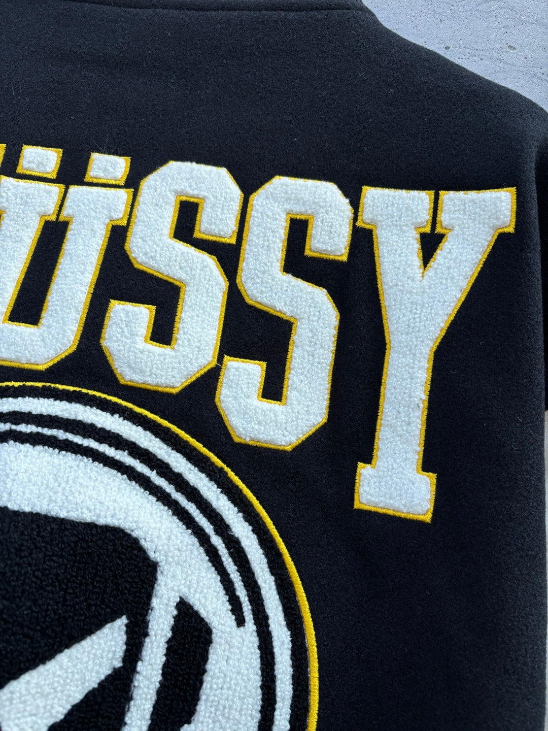 Black Stussy jacket back close-up of raised lettering and circular logo edge