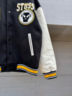 Black varsity jacket sleeve close-up with circular skull logo and long white stripe