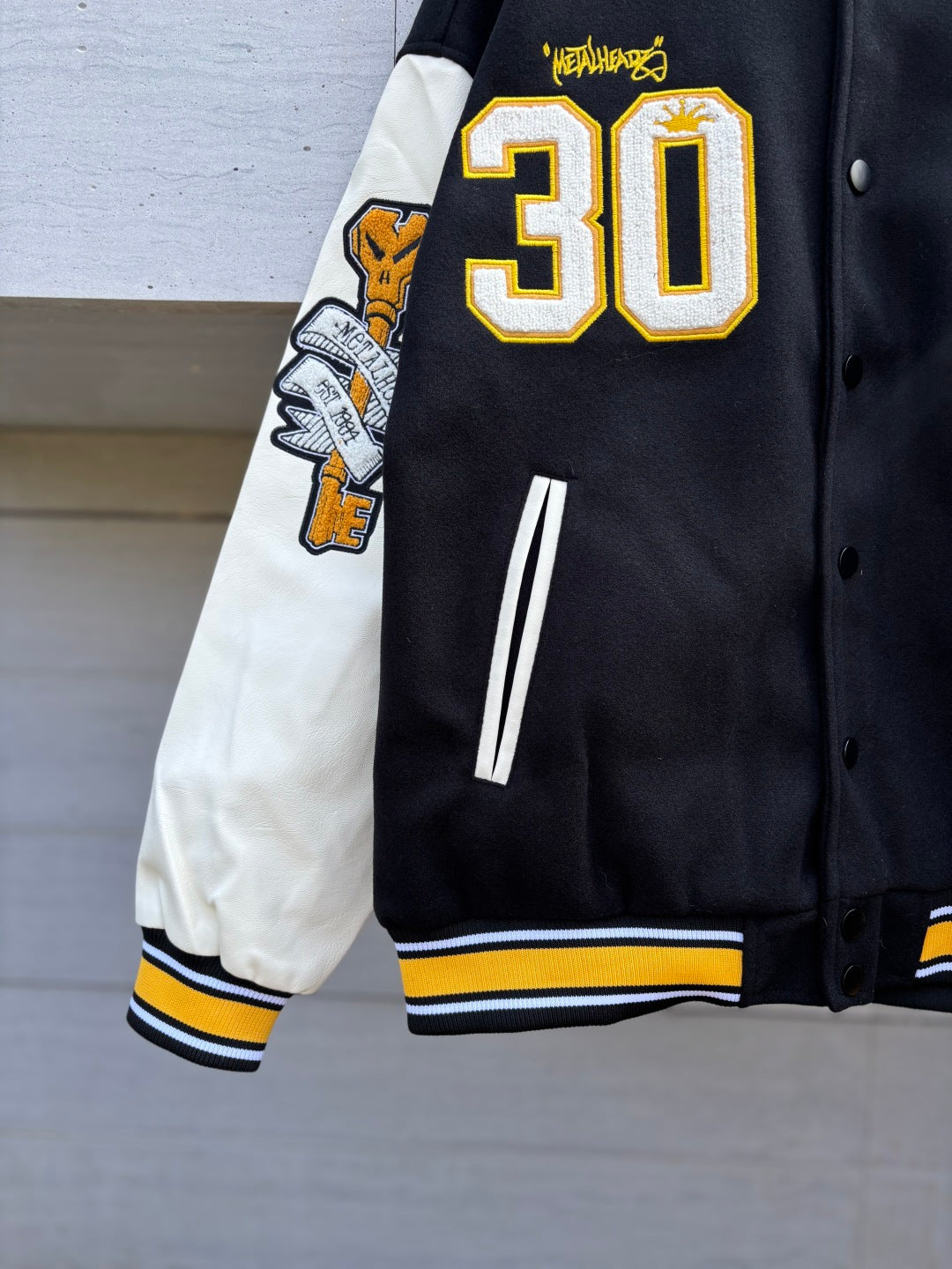 Black varsity jacket side view with 30 patch sleeve, white striped accents and cuffs