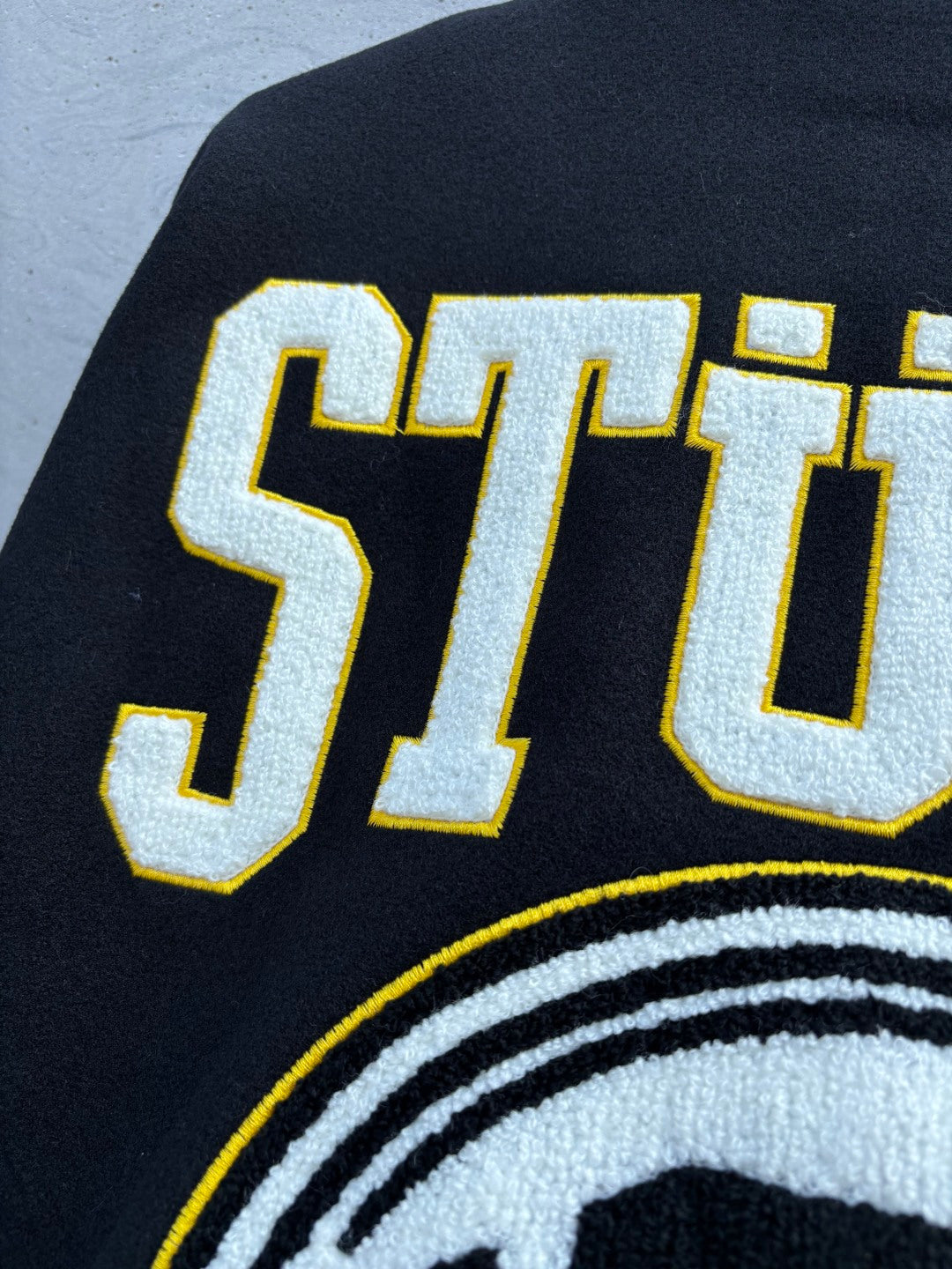 Black Stussy jacket back with bold yellow outlined lettering and circular emblem