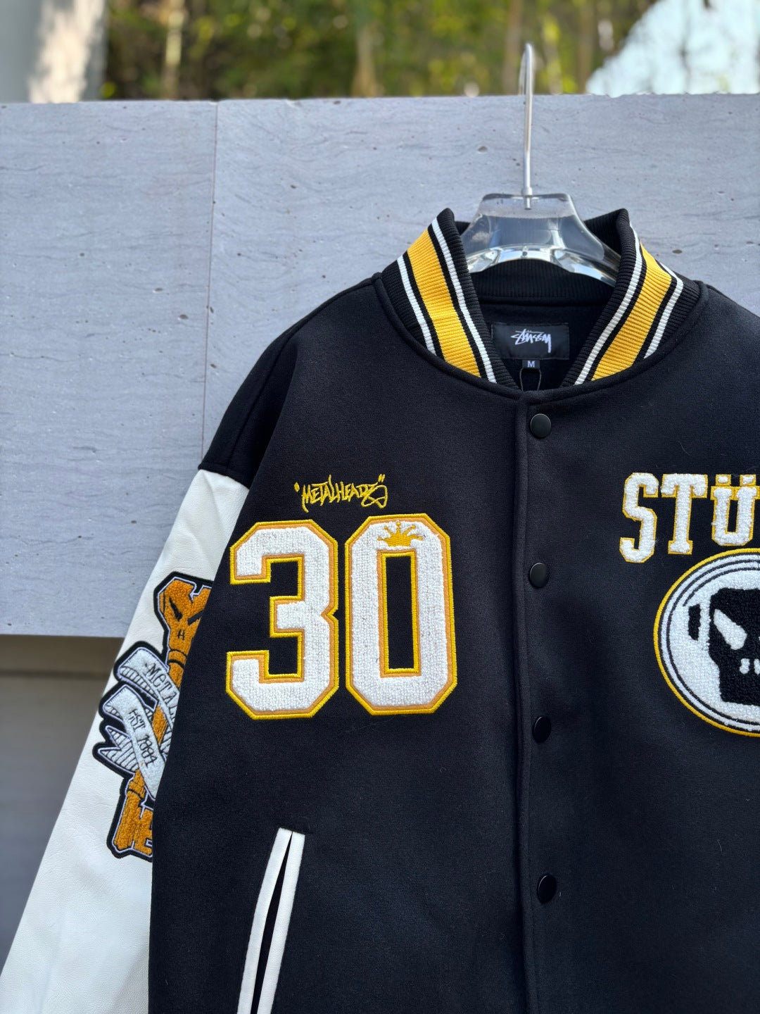 Black varsity jacket front close-up with 30 graphic, STUSSY patch, striped collar trim
