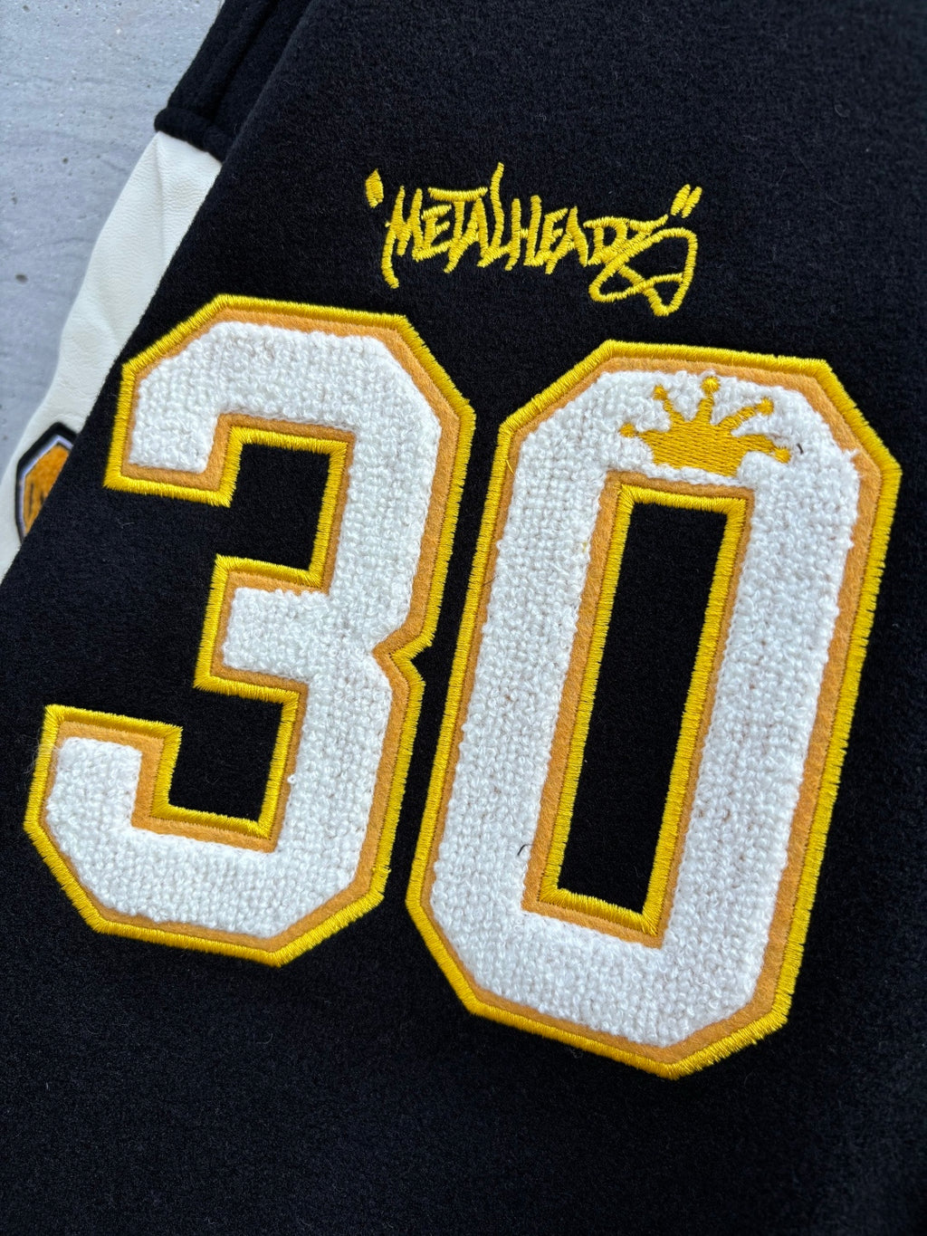 Black varsity jacket graphic patch detail showing large 30 numbers and yellow outline
