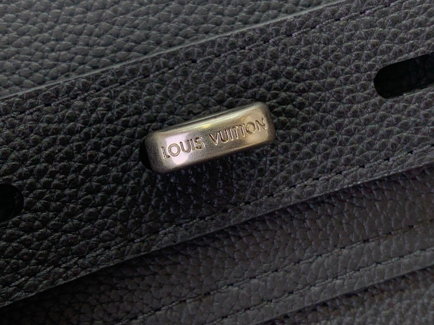 Louis Vuitton bag clasp with engraved logo on dark leather