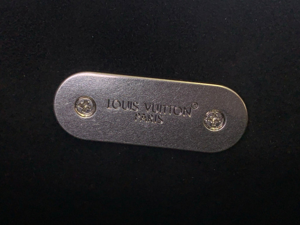 Louis Vuitton backpack close-up of gold-toned metal logo plate on dark leather