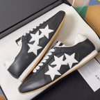 Black leather sneakers with white star appliques and gum soles, side-by-side in box