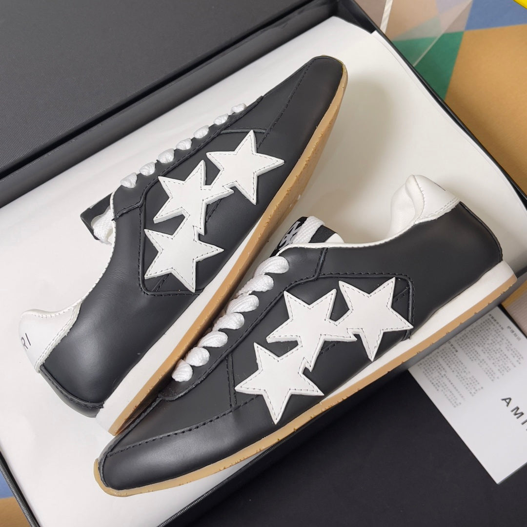 Black leather sneakers with white star appliques and gum soles, side-by-side in box