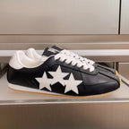 Black leather sneakers with white star appliques, white laces, and gum sole