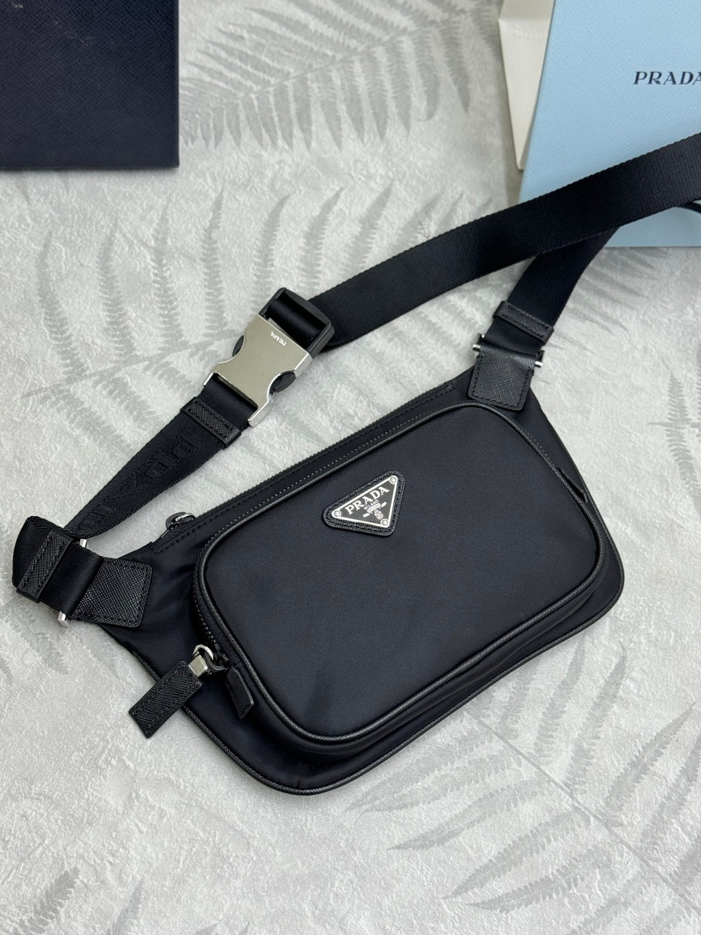 Black Prada crossbody bag with adjustable webbing strap, front logo patch, and zip pull.