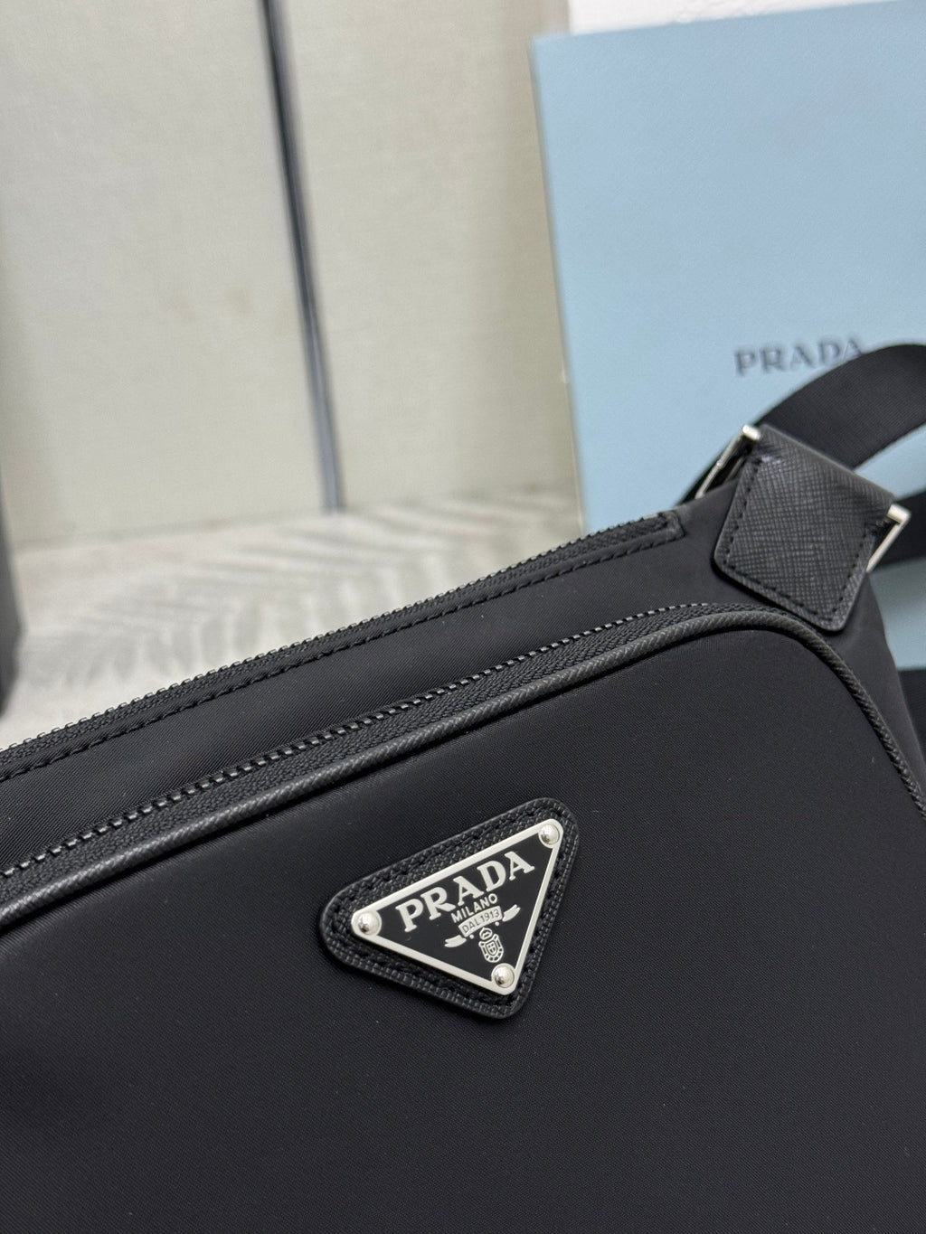 Black Prada crossbody bag close-up: triangular logo patch on front panel and stitching.