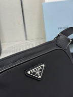 Black Prada crossbody bag close-up: triangular logo patch on front panel and stitching.