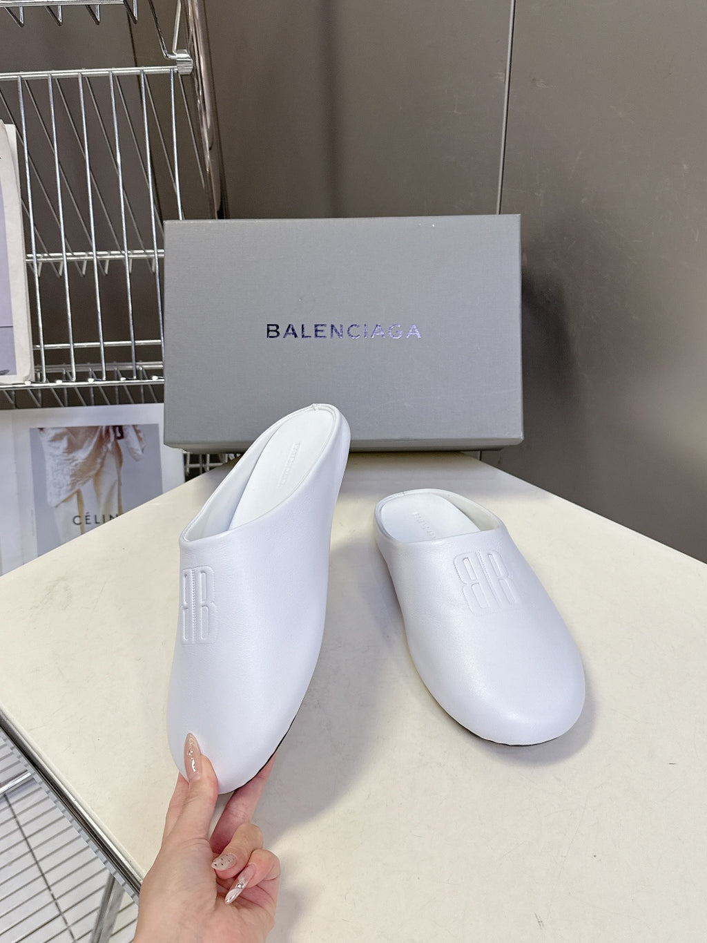 White slide sandals with embossed logo, held by hand