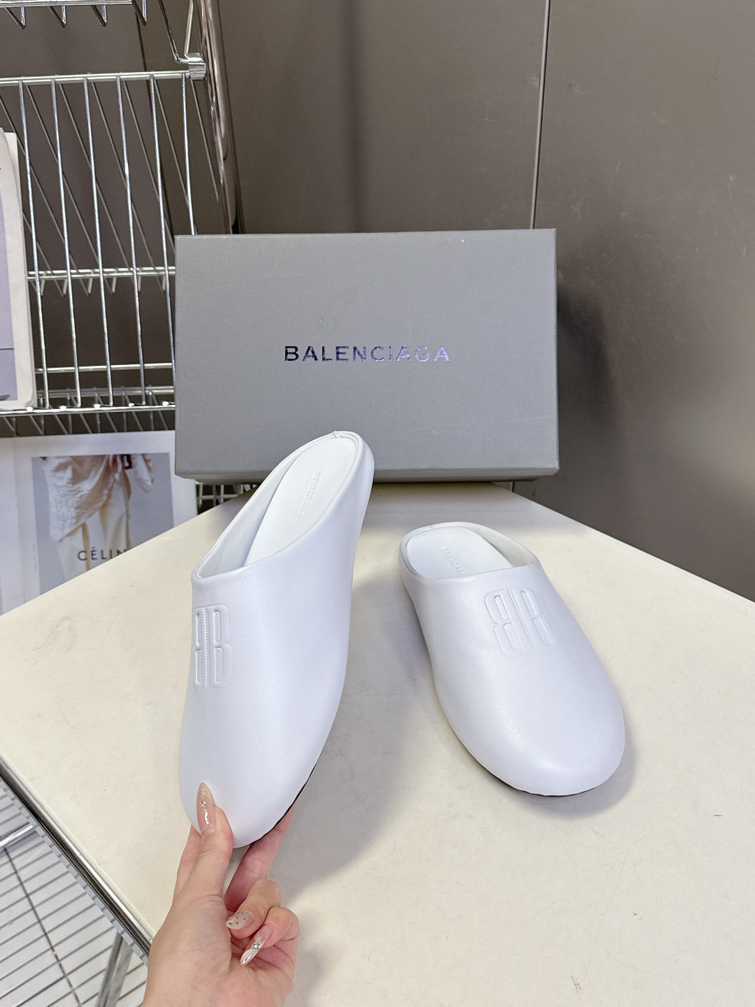 White slide sandals with embossed logo, held by hand