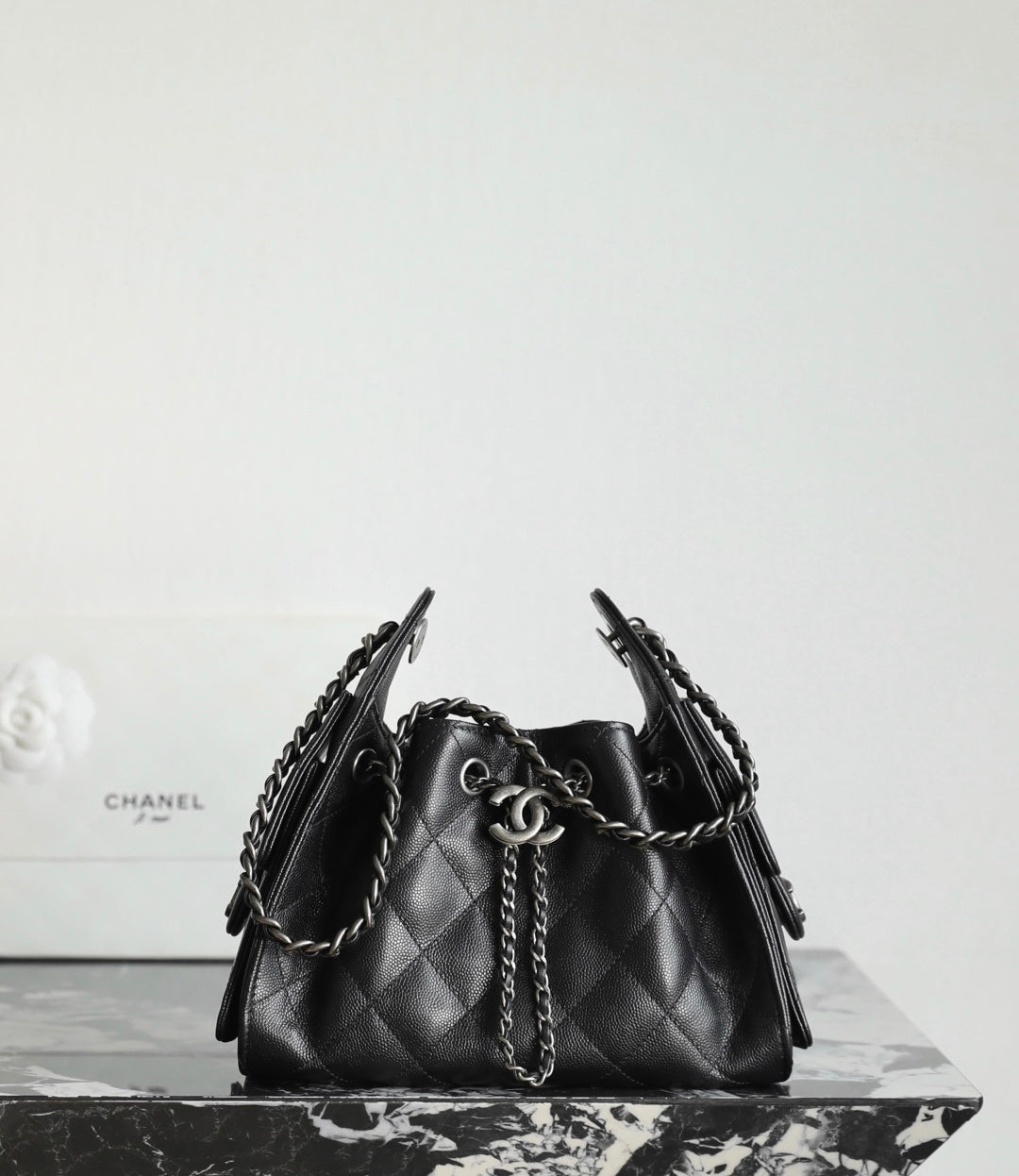 Black quilted bucket bag with chain strap handles and CC charm on the front