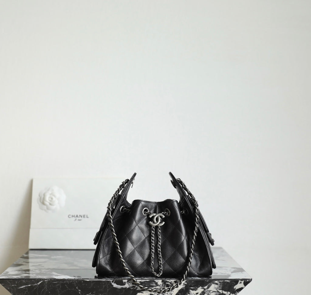 Black quilted bucket bag with chain handles and CC charm at the drawstring front