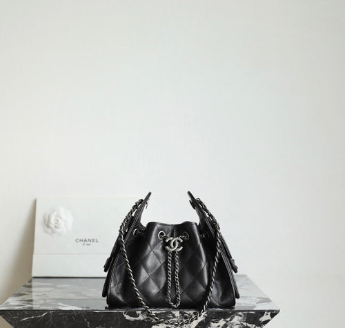 Black quilted bucket bag with chain handles and CC charm at the drawstring front