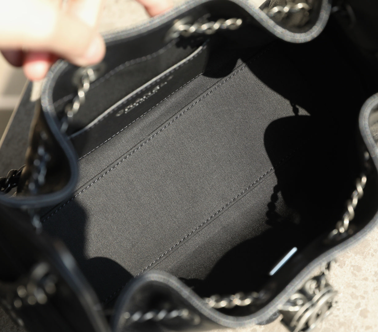 Black fabric-lined interior of a bag with stitched edge and metal chain hardware