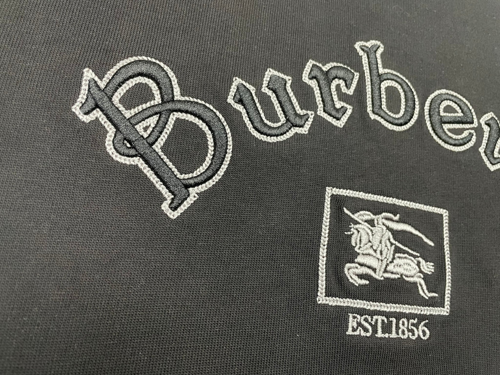 Large embroidered Burberry wordmark and horse crest with EST1856 on black T-shirt.