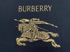Dark T-shirt chest graphic with gold “BURBERRY” text and horse rider logo