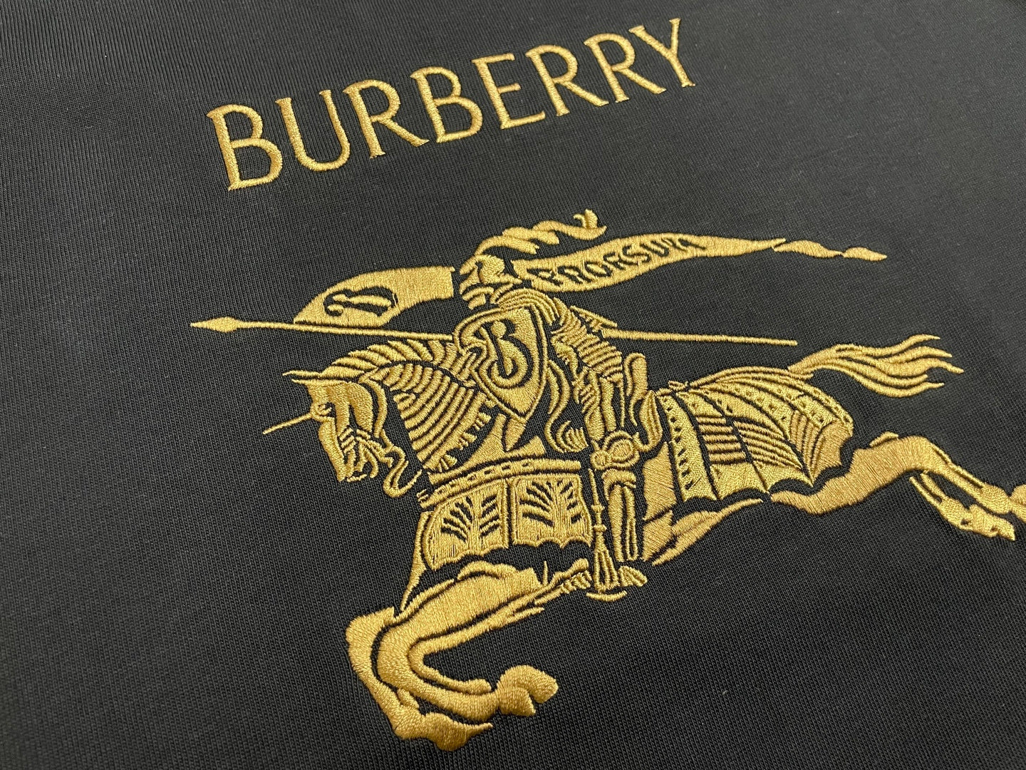 Black T-shirt chest graphic with gold “BURBERRY” text and horse rider logo