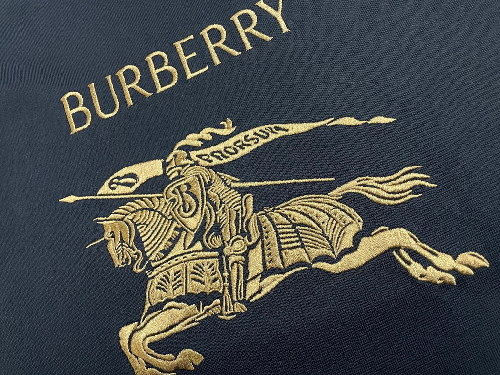 Navy T-shirt chest graphic with gold “BURBERRY” text and horse rider logo