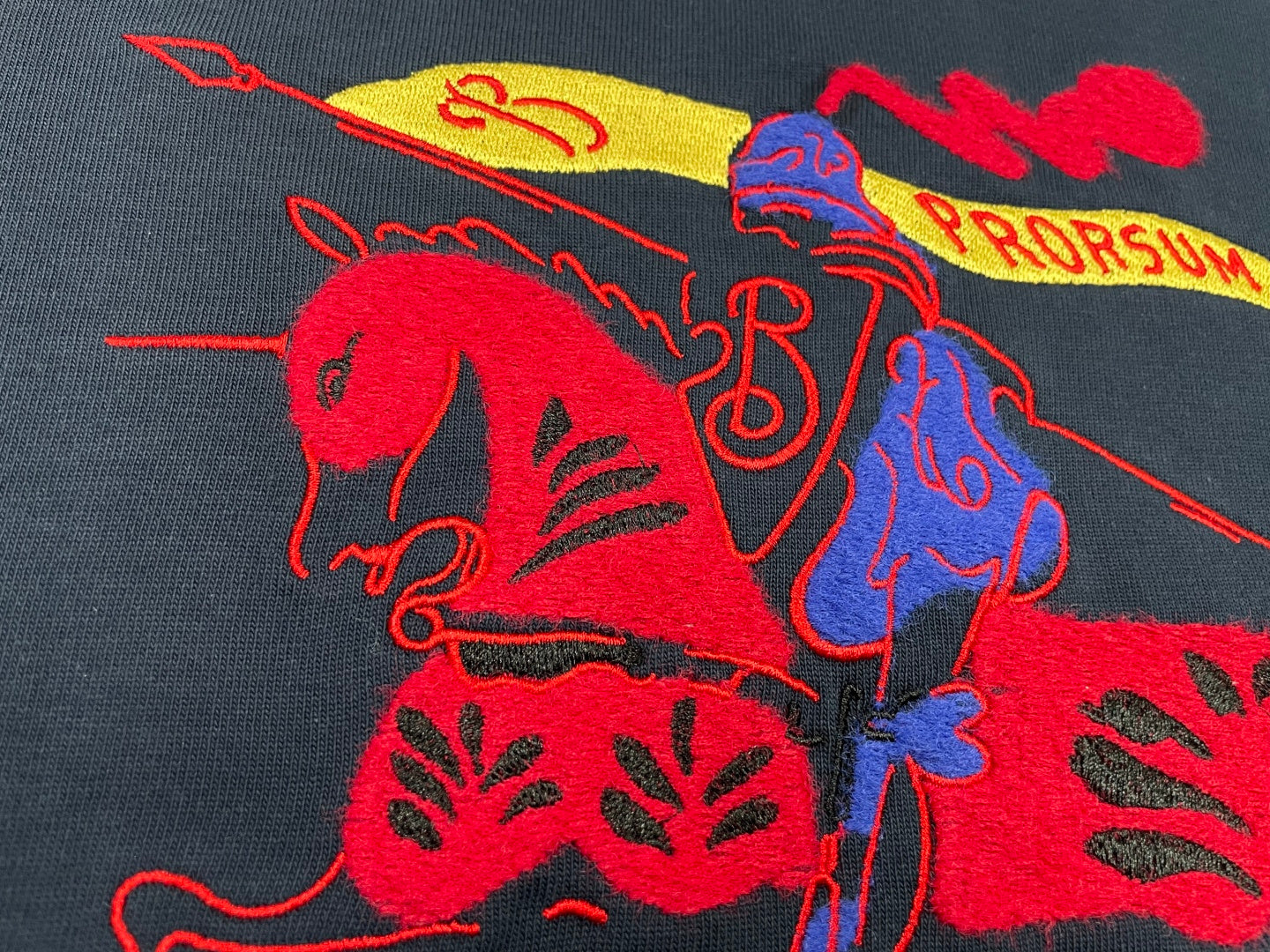 Navy T-shirt close-up of red and blue graphic horse-style print with yellow accents.