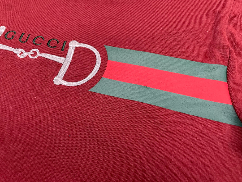 Red T-shirt chest with partial white horsebit graphic and green stripe