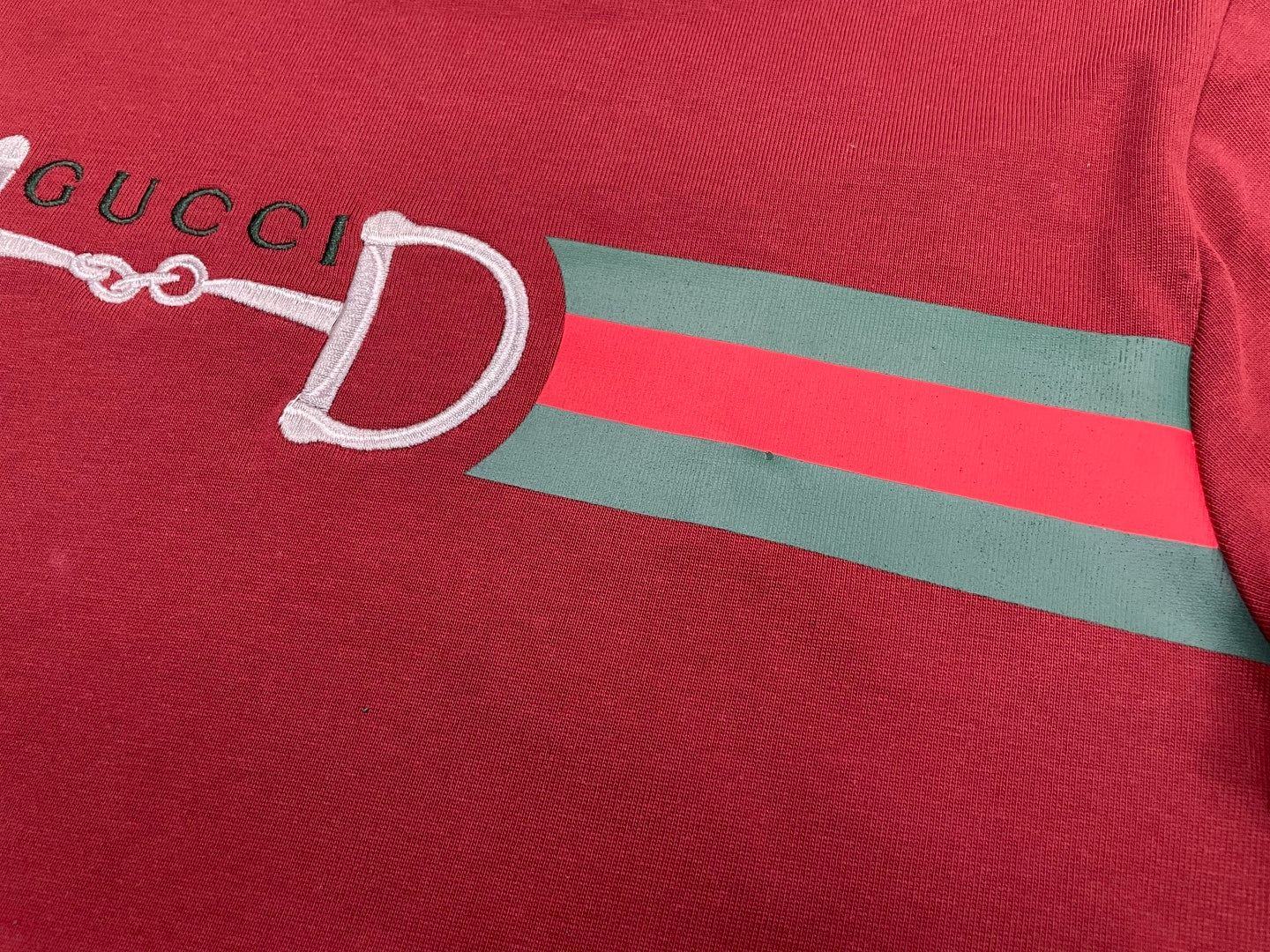 Red T-shirt chest with partial white horsebit graphic and green stripe