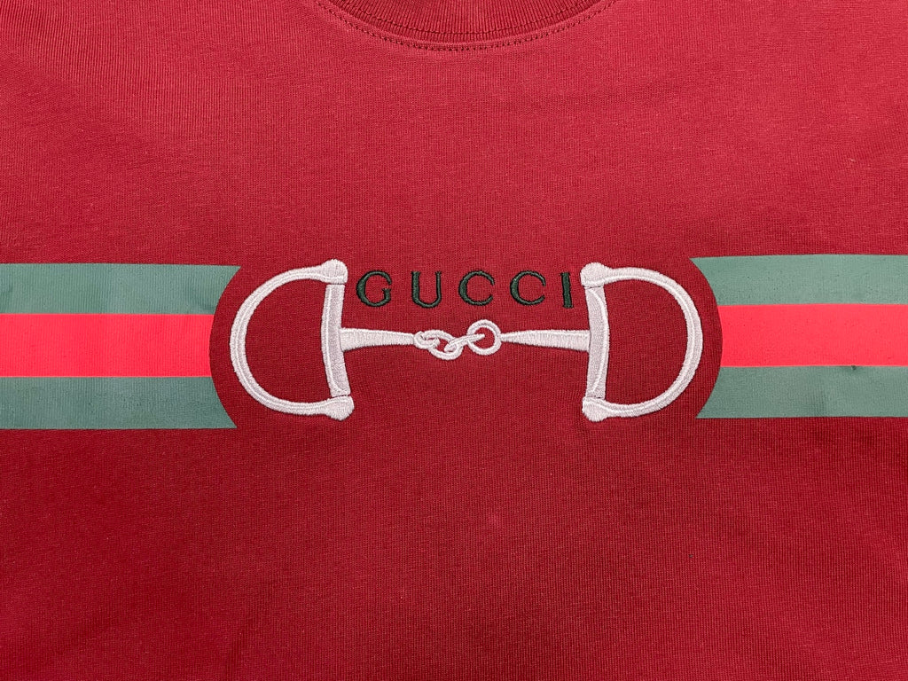 Red T-shirt front with large white horsebit graphic and Gucci lettering