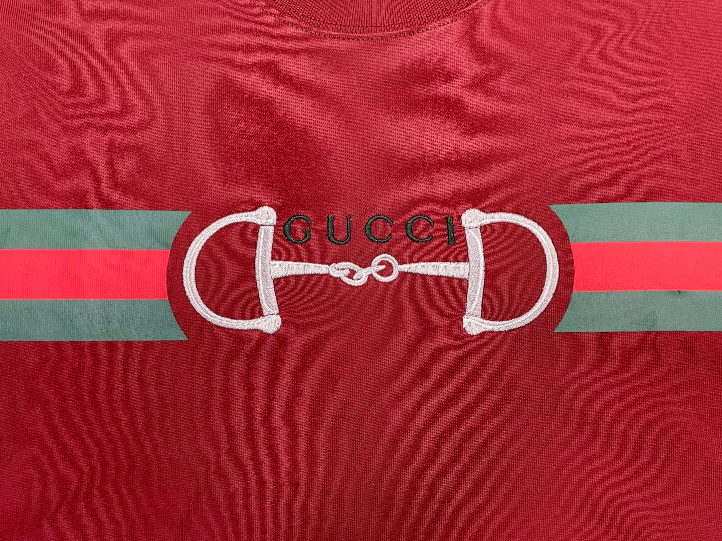 Red T-shirt front with large white horsebit graphic and Gucci lettering