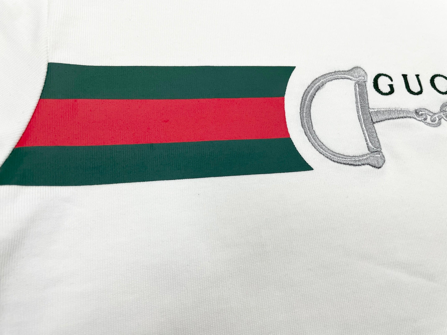 White T-shirt hem with green and red stripe band and horsebit graphic