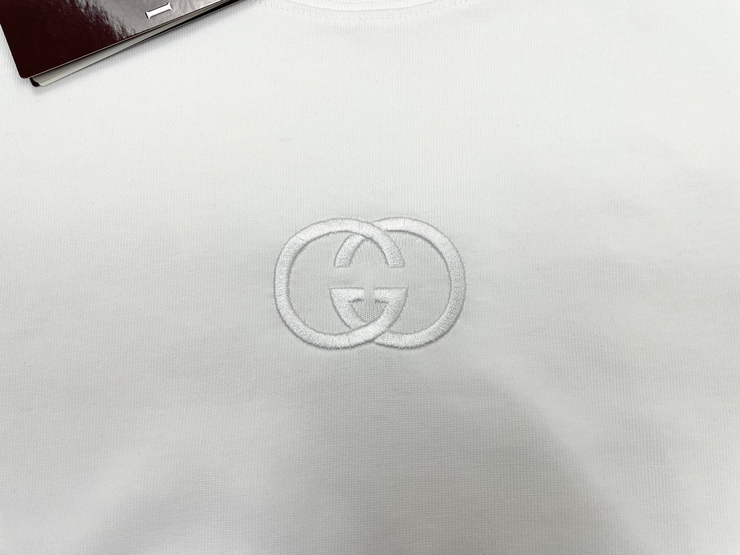 White short-sleeve T-shirt with metallic GG logo emblem at center