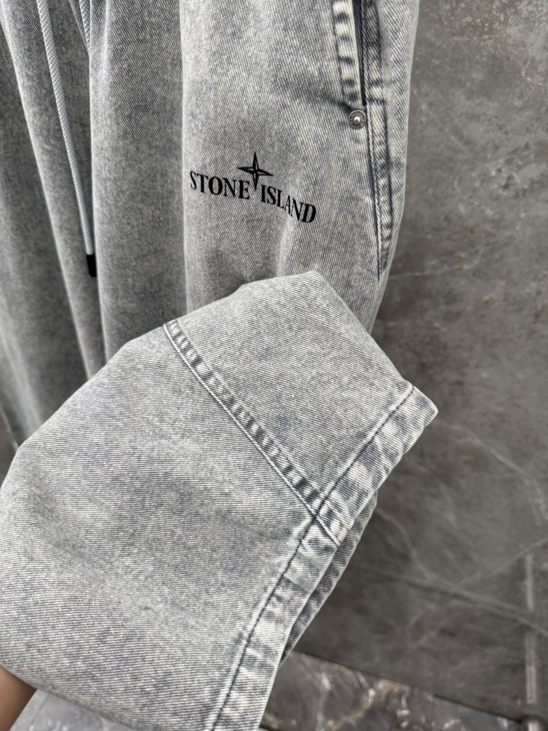 Grey denim jogger pants close-up with logo graphic and stitched cuff