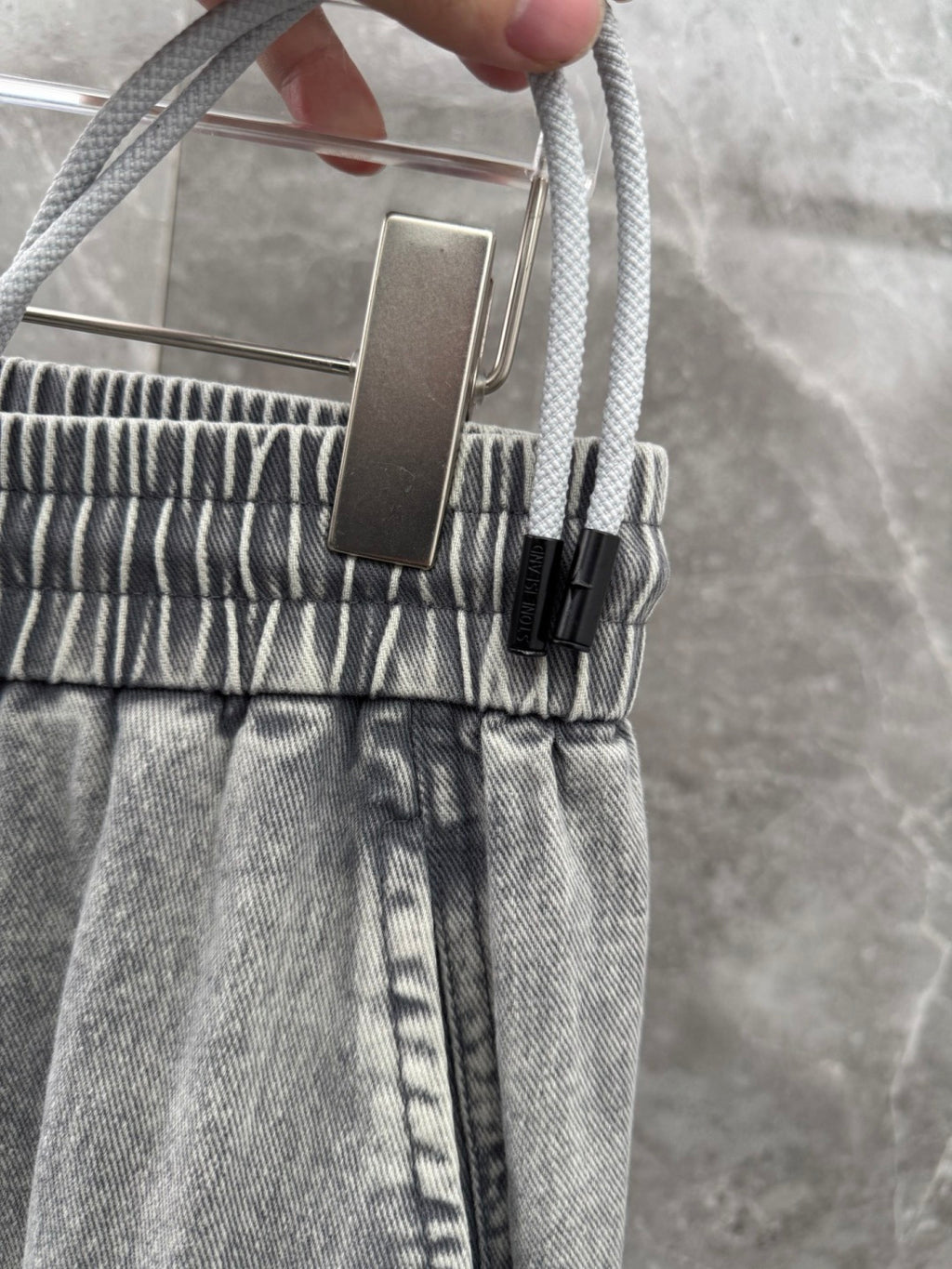 Grey denim jogger pants close-up with adjustable drawstring and ribbed waistband
