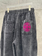 Washed gray denim pants with pink circular logo patch on back right pocket.