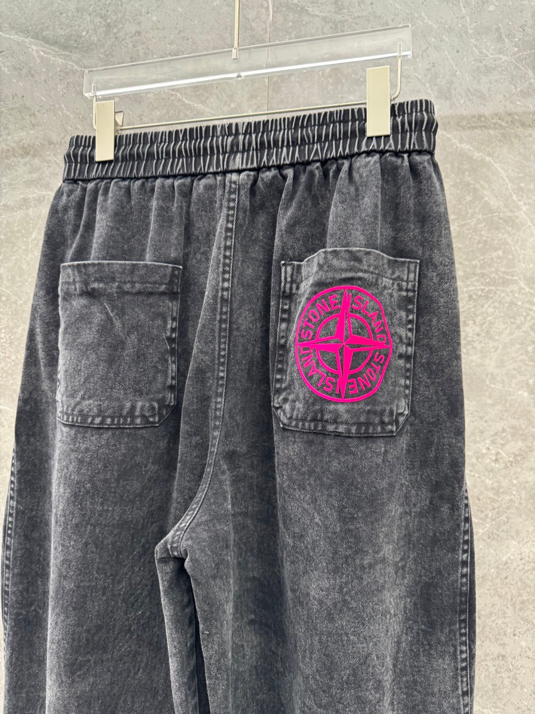 Washed gray denim pants with pink circular logo patch on back right pocket.