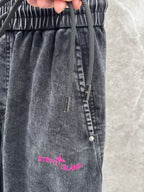 Washed gray denim pants close-up: elastic waistband, drawstring, and pink Stone Island text.