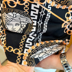 Black polo shirt sleeve close-up with Medusa print, geometric trim, and gold chain accents.