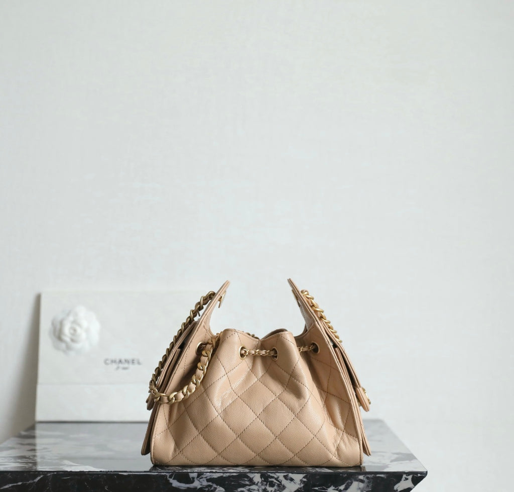 Chanel beige bucket bag with quilted sides, top clasp, and dual chain straps.