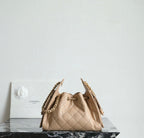 Chanel beige bucket bag with quilted sides, top clasp, and dual chain straps.