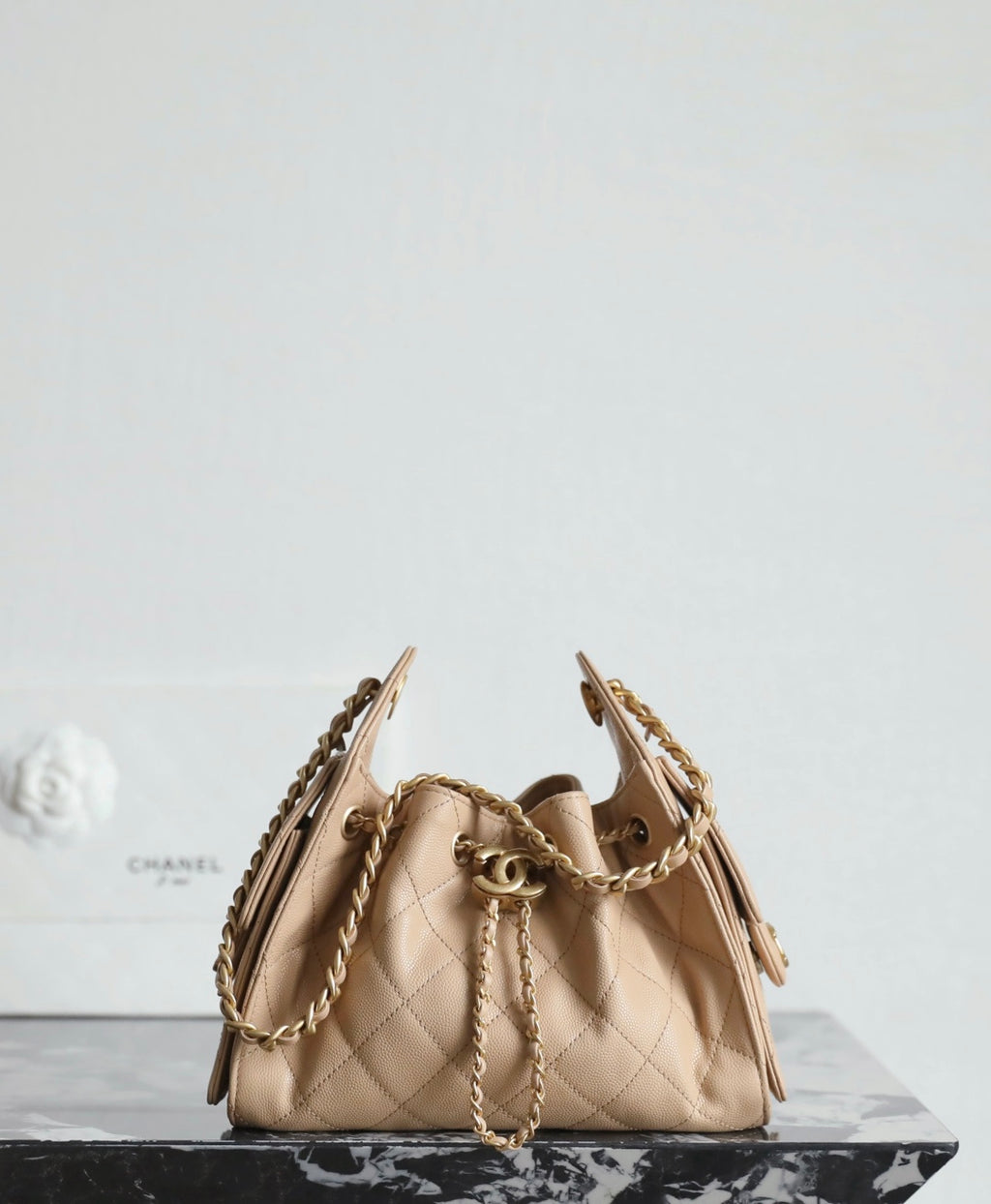 Chanel beige bucket bag with quilted pattern, gold hardware, and chain shoulder straps.