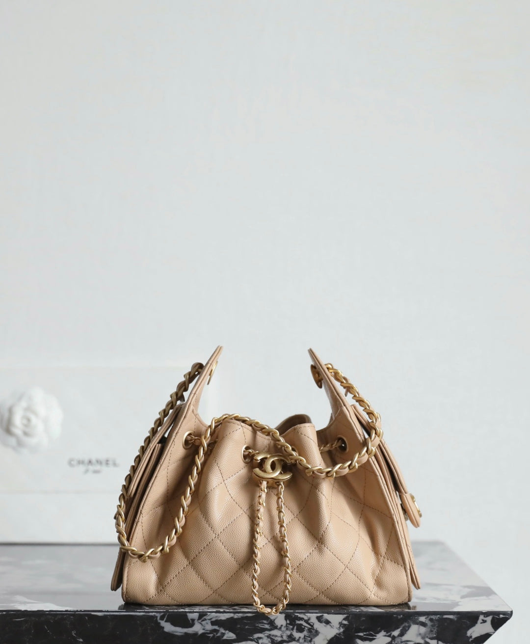 Chanel beige bucket bag with quilted pattern, gold hardware, and chain shoulder straps.