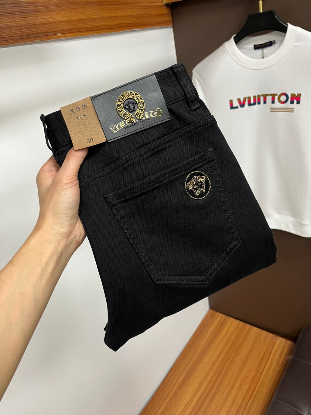 Black pants with gold logo button and front fly, folded at the waist in hand