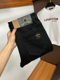 Black pants with gold logo button and front fly, folded at the waist in hand