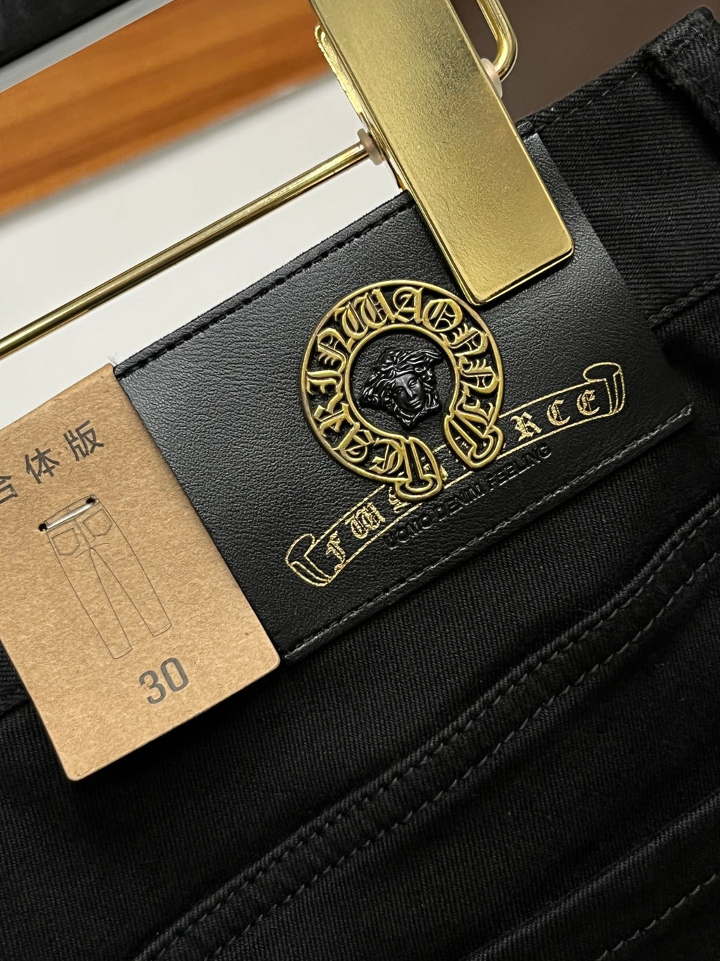 Black pants pocket and belt detail with gold logo patch and leather tag