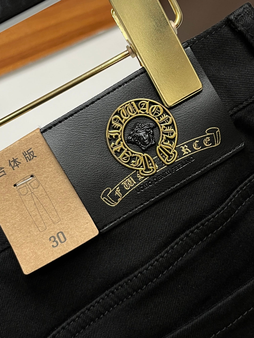 Black pants pocket and belt detail with gold logo patch and leather tag