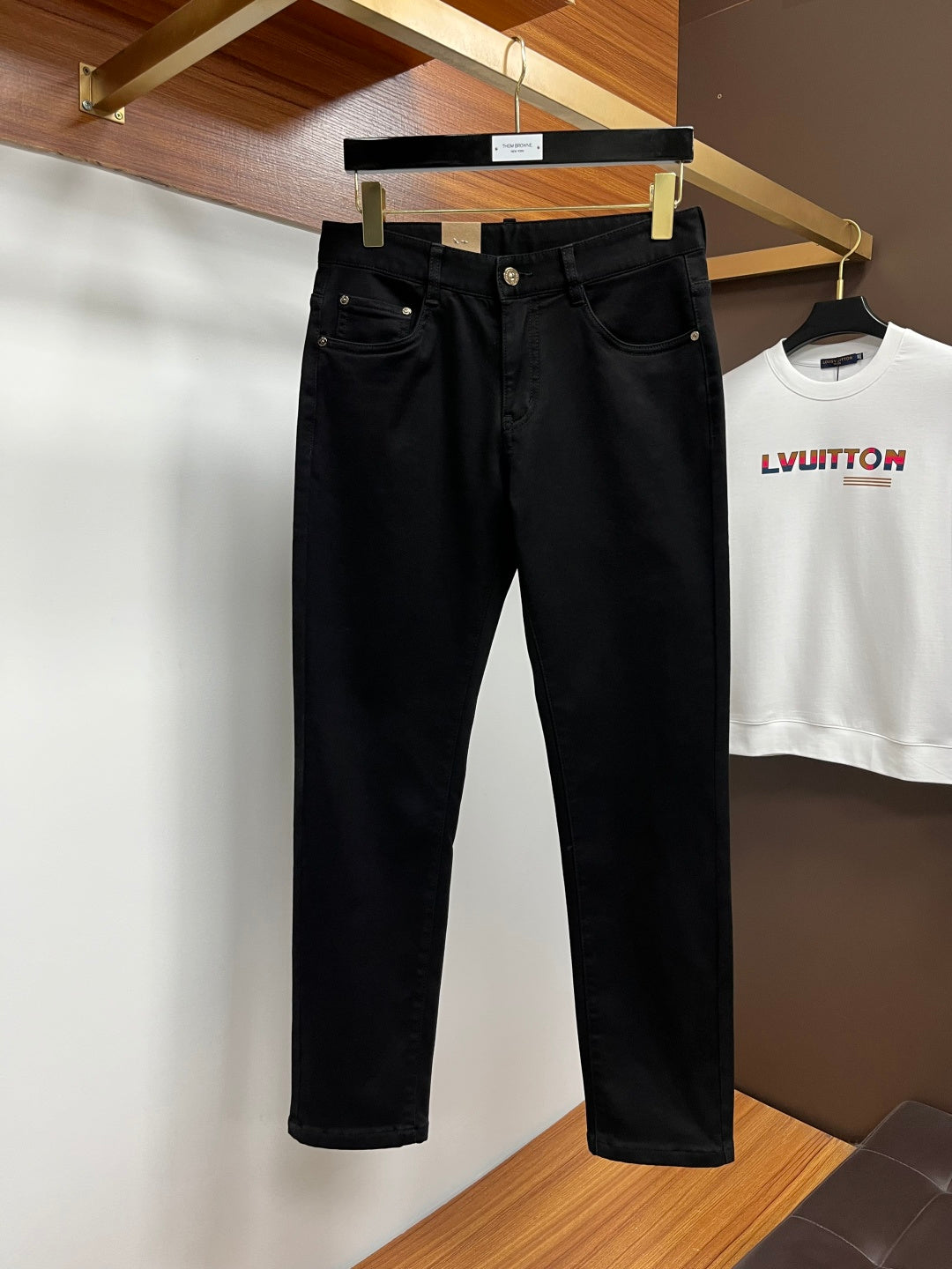 Black pants hanging on a rack, straight legs with front button and belt loops