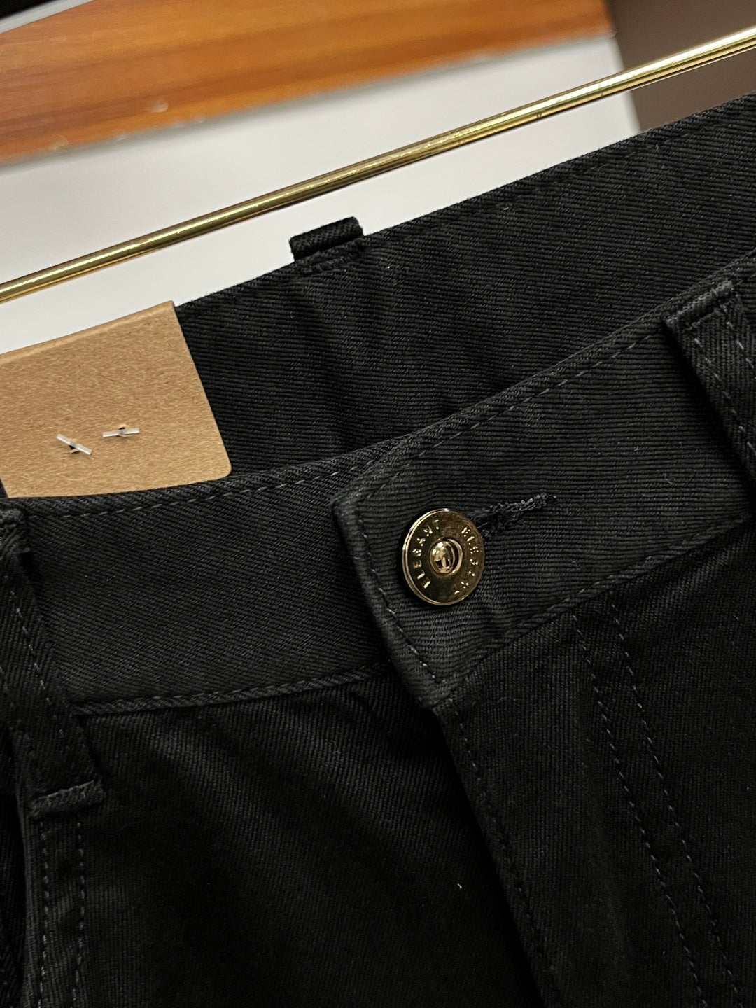 Black pants waistband and side seam with small gold emblem button