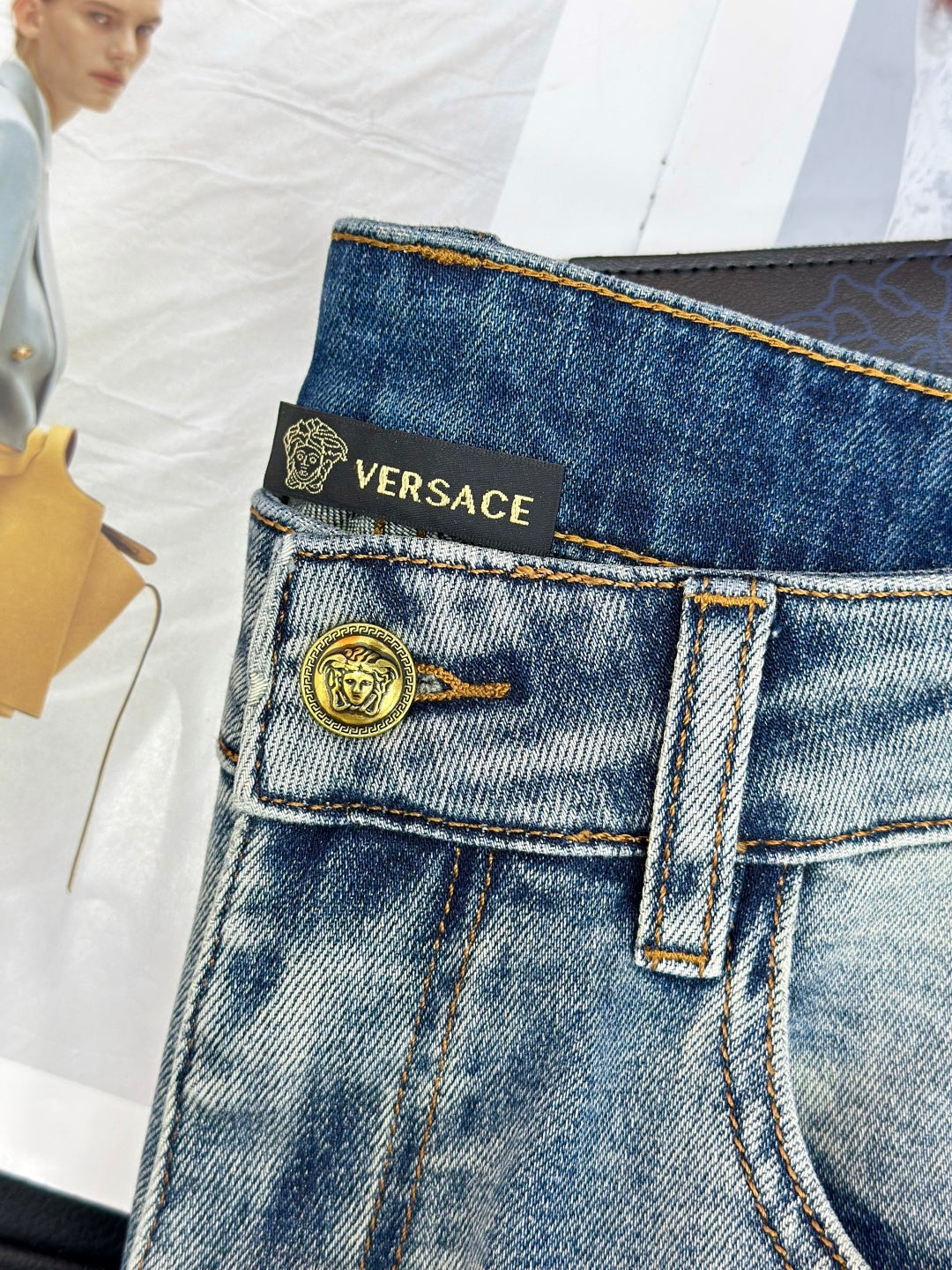 Light-wash denim jeans with gold button, VERSACE waistband text, and belt loops