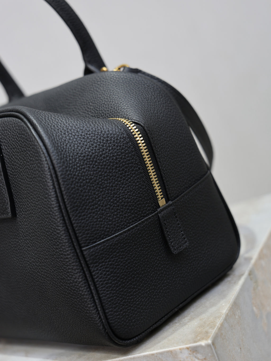 Black handbag with gold zipper detail and front seam panel, pebbled texture