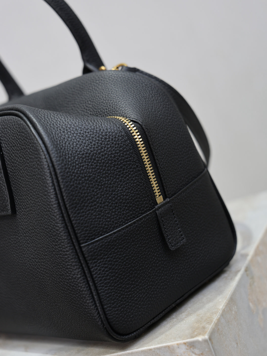 Black handbag with gold zipper detail and front seam panel, pebbled texture